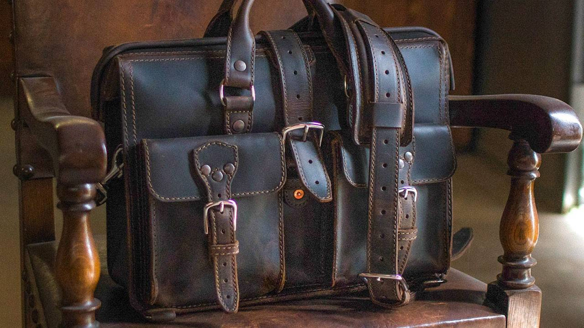 Dark brown leather briefcase with buckle straps resting on an antique wooden chair