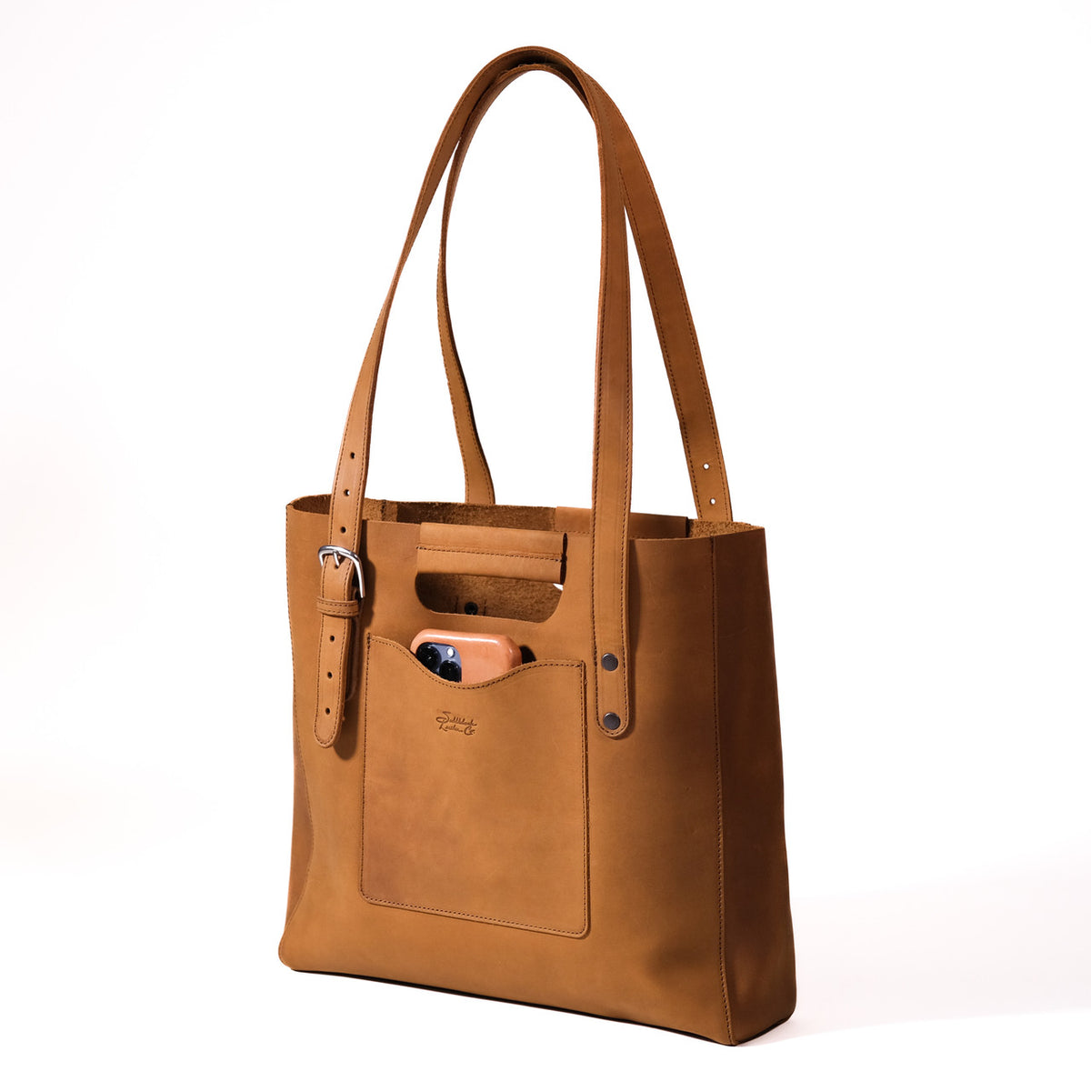 Everyday Leather Tote in Tobacco, angled front view with shoulder handles, buckled side strap and a phone in the front pocket