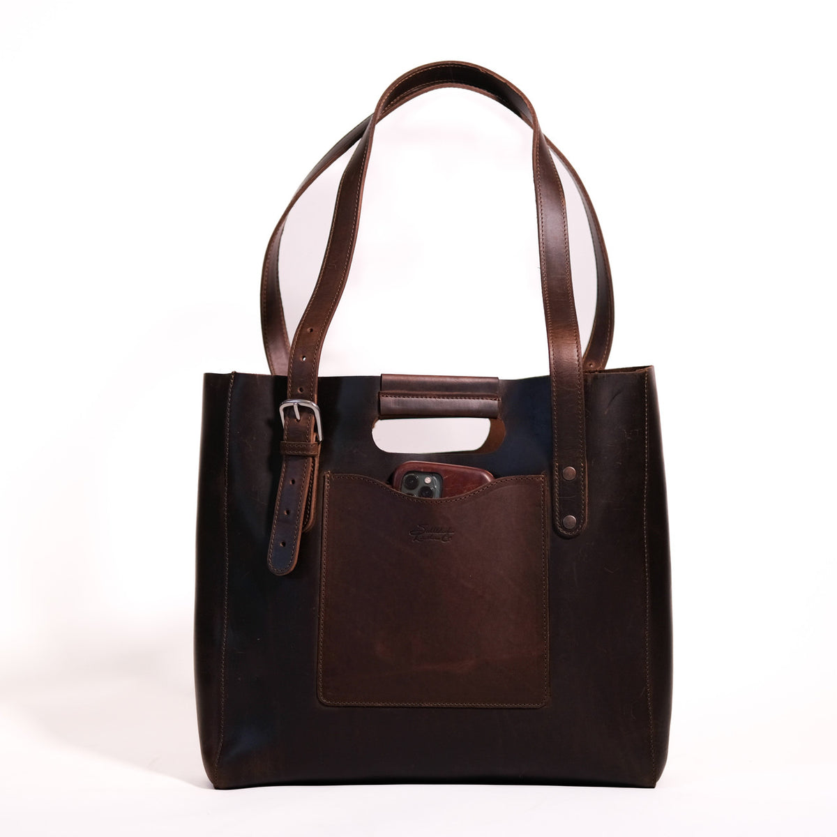 Everyday Leather Tote in Dark Coffee Brown, front view with shoulder handles, buckled side strap and a phone in the front pocket