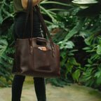 Urban Leather Tote in Chestnut carried on the shoulder by a woman walking past tropical plants