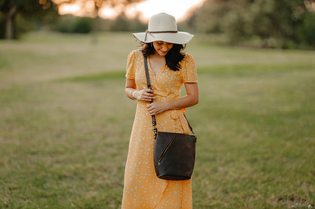 Crossbody Concealed Leather Bag in Black, worn by a woman in a yellow dress and sun hat in a field