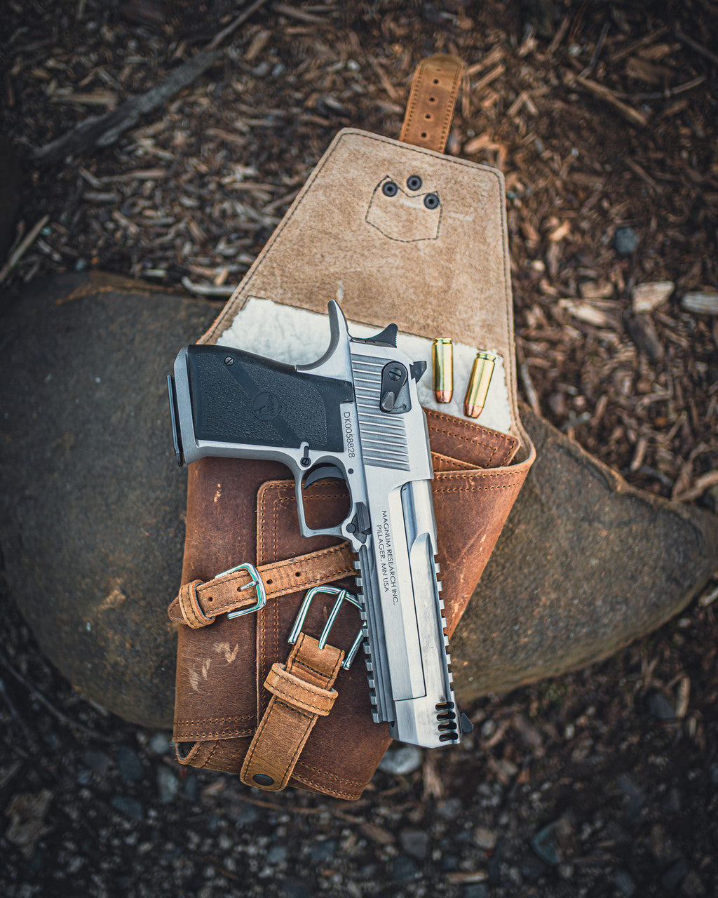Leather Pistol Wrap in Tobacco opened on a rock with a stainless pistol and cartridges tucked inside