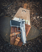 Leather Pistol Wrap in Tobacco opened on a rock with a stainless pistol and cartridges tucked inside