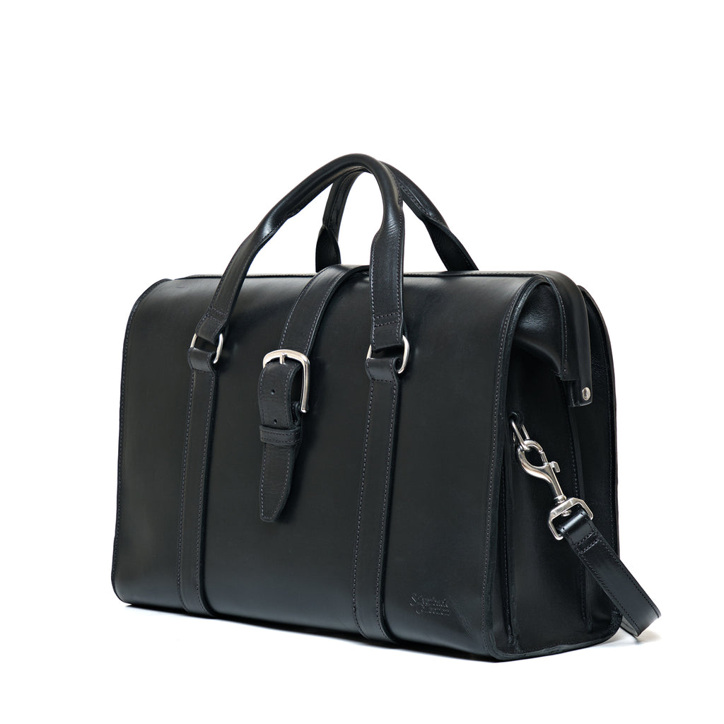 Spurgeon Briefcase in Raven Black, angled side view showing the buckle strap and shoulder strap clip
