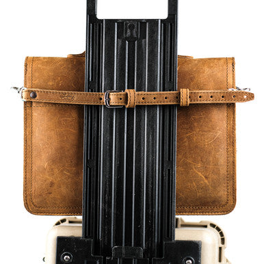 Leather Luggage Strap in Tobacco buckled around a leather bag to secure it to a rolling suitcase handle
