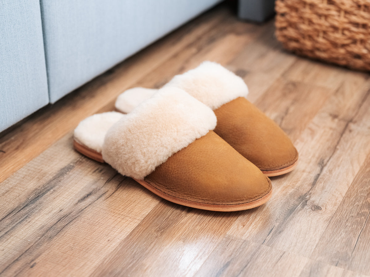 Women's Sheepskin Slippers in Tan, pair with fluffy sheepskin cuffs on a wooden floor