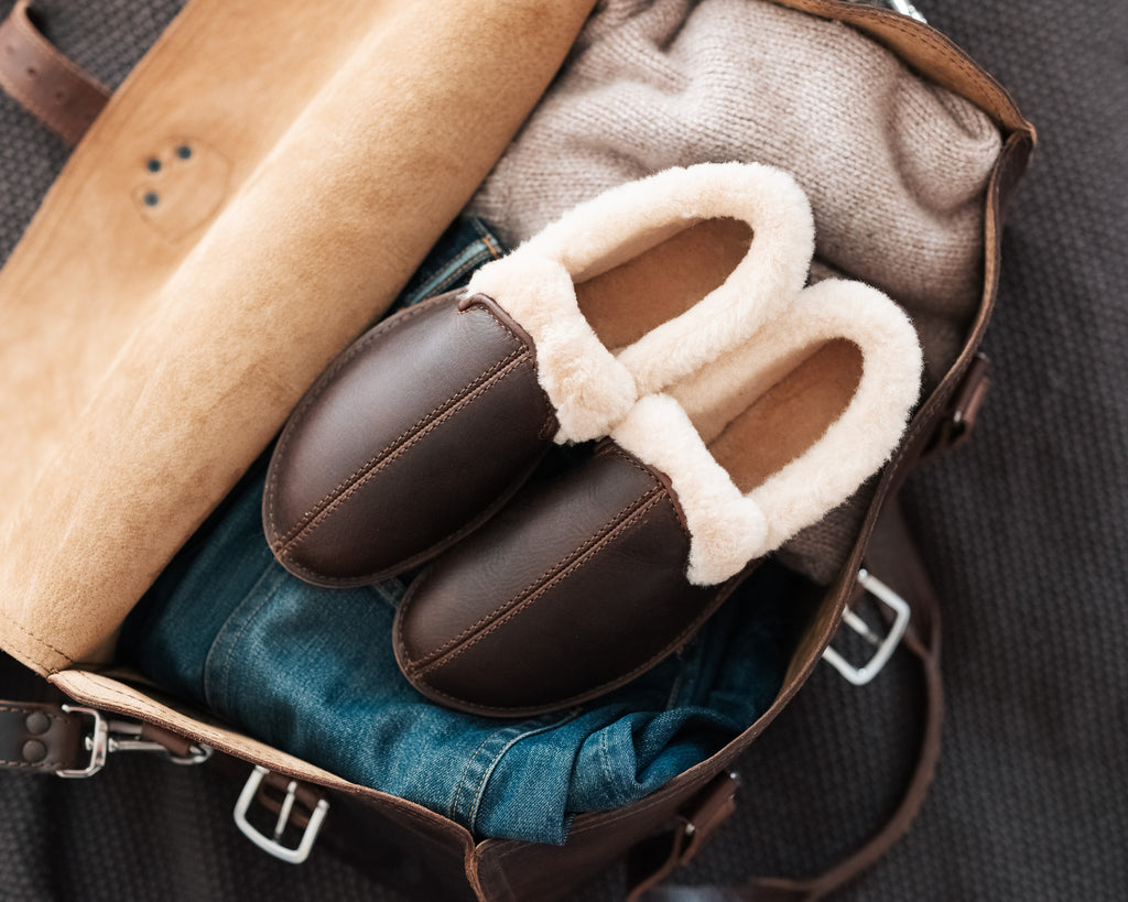 Pair of Sheepskin Moccasins in Dark Coffee Brown with cream shearling lining, packed in an open leather bag with jeans