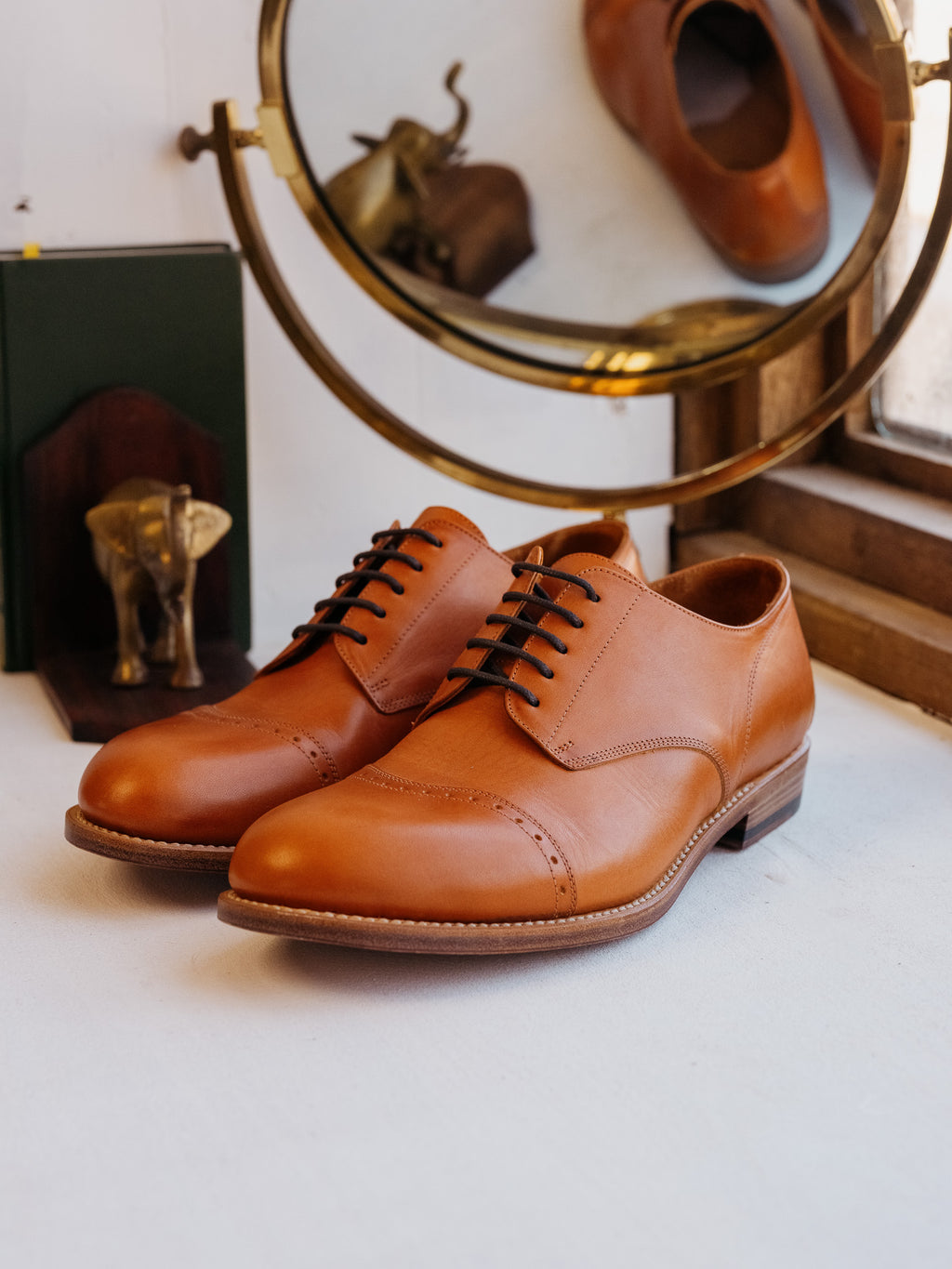 Toe Cap Shoes in English Tan, pair beside a brass mirror and elephant bookend