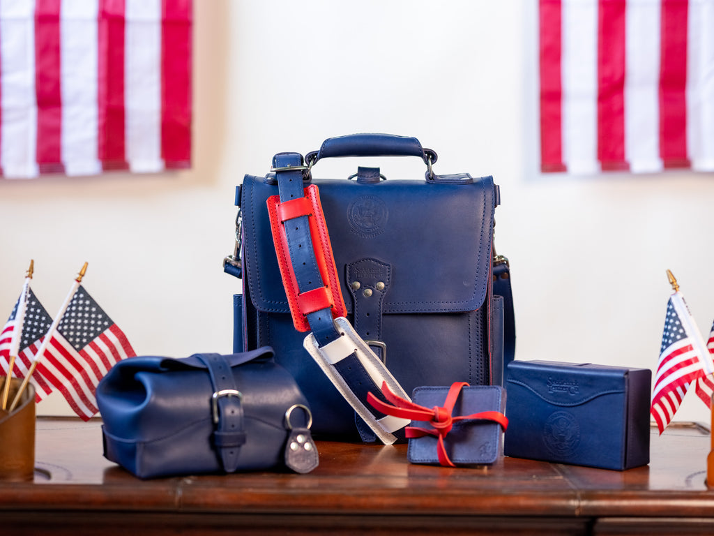 Saddleback Club Membership, navy blue leather bag and accessories with red straps displayed among American flags
