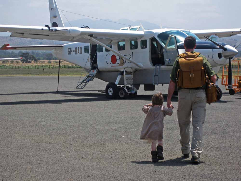 Tank Backpack in Tobacco, worn by a man walking with a small child toward a bush plane