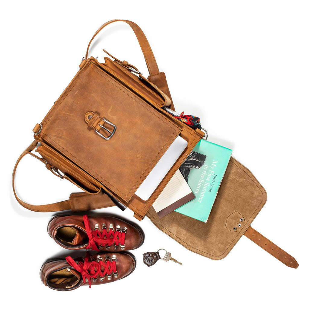 Tank Backpack in Tobacco, top view open with books spilling out beside hiking boots and keys