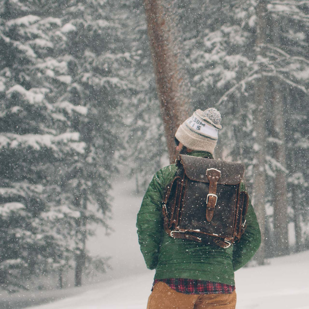 Tank Backpack in Dark Coffee Brown, worn by a man walking through a snowy pine forest