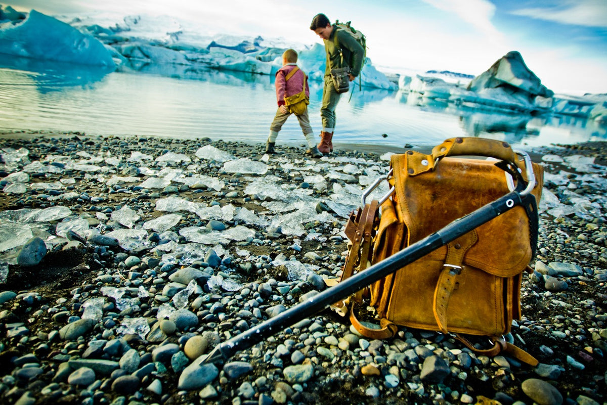Tank Backpack in Tobacco on a rocky glacier lagoon beach, with a man and child walking behind
