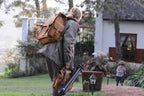 Tank Backpack in Tobacco, carried by a woman with a tripod as a child runs across a garden
