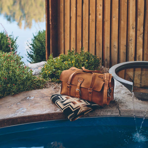 20" Baby Beast Duffle Bag in Tobacco on a patterned blanket at the edge of a poolside water feature