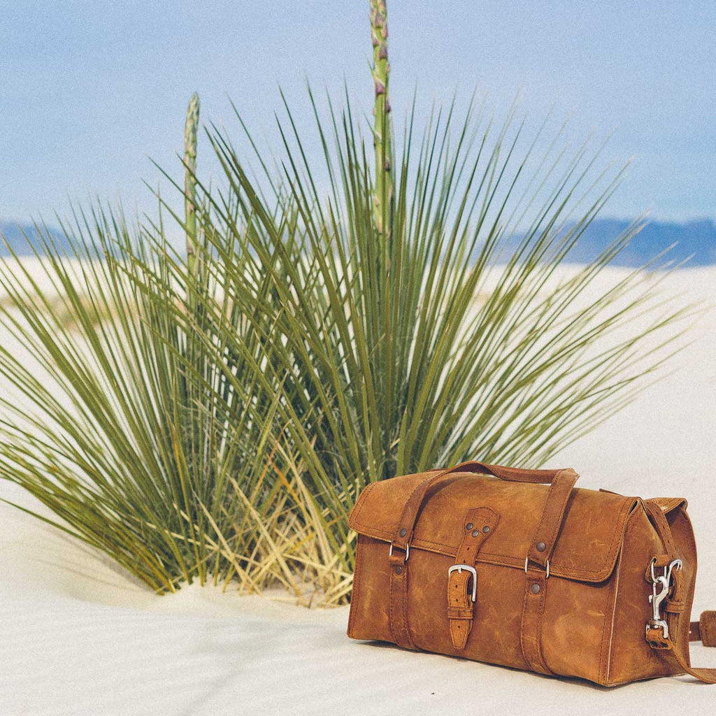 20" Baby Beast Duffle Bag in Tobacco resting on white sand beside a desert yucca plant