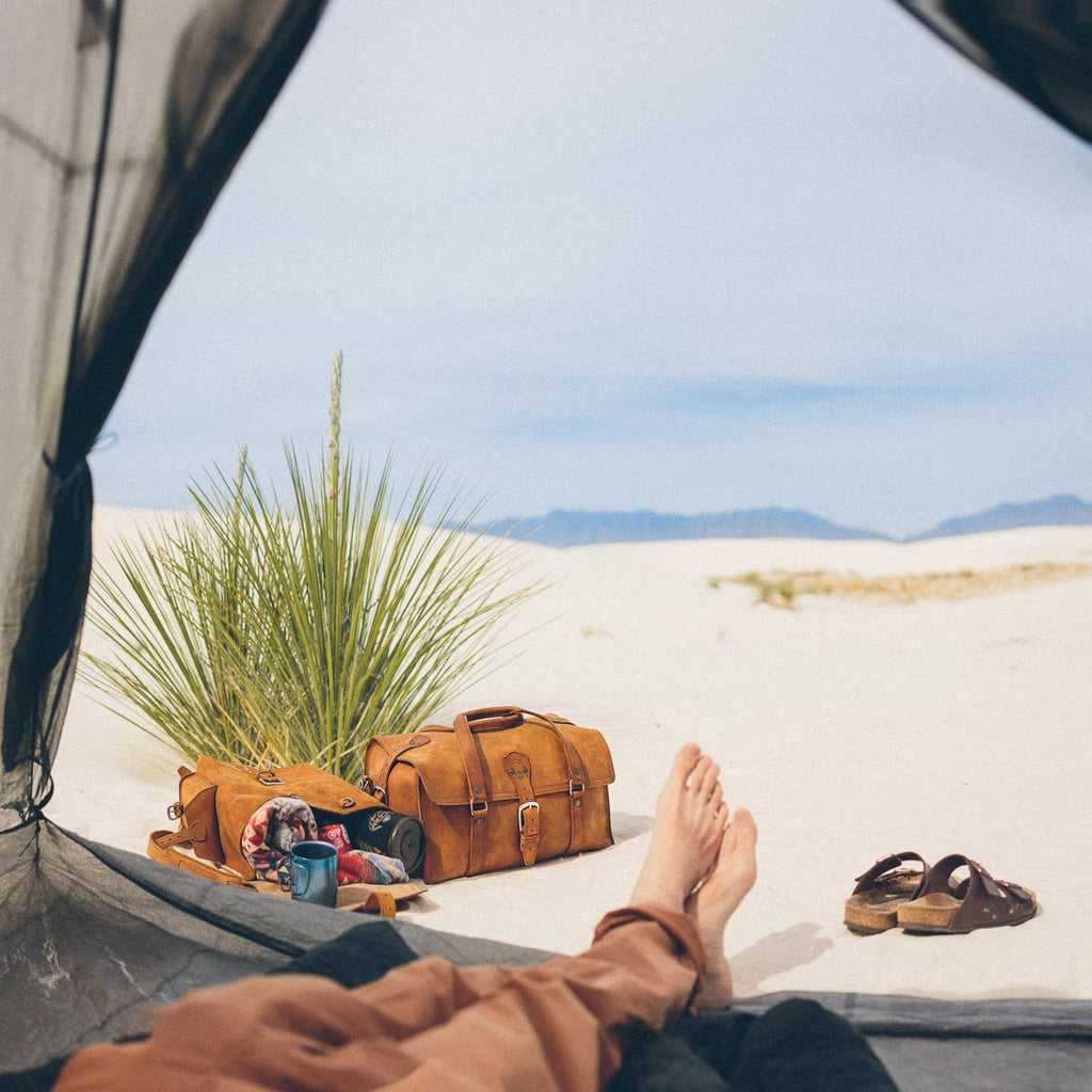 20" Baby Beast Duffle Bag in Tobacco on white sand dunes, seen from inside a tent past bare feet