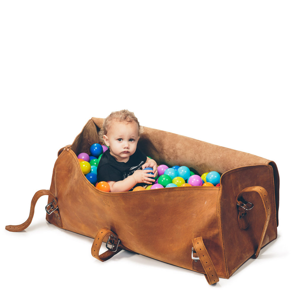 34" Beast Duffle Bag in Tobacco, open with a toddler sitting inside among colorful play balls to show its size