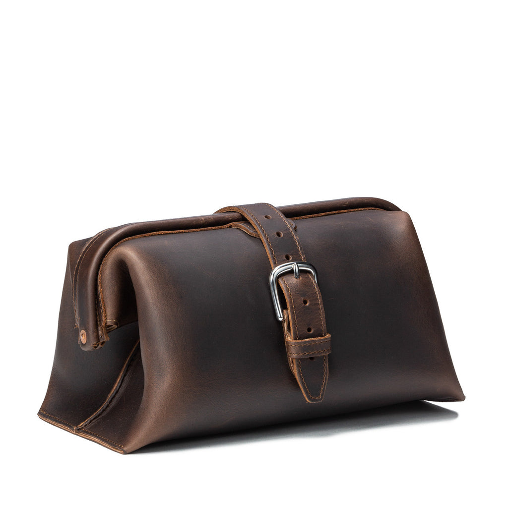 Big Mouth Leather Toiletry Bag in Dark Coffee Brown, angled front view with buckle strap closure