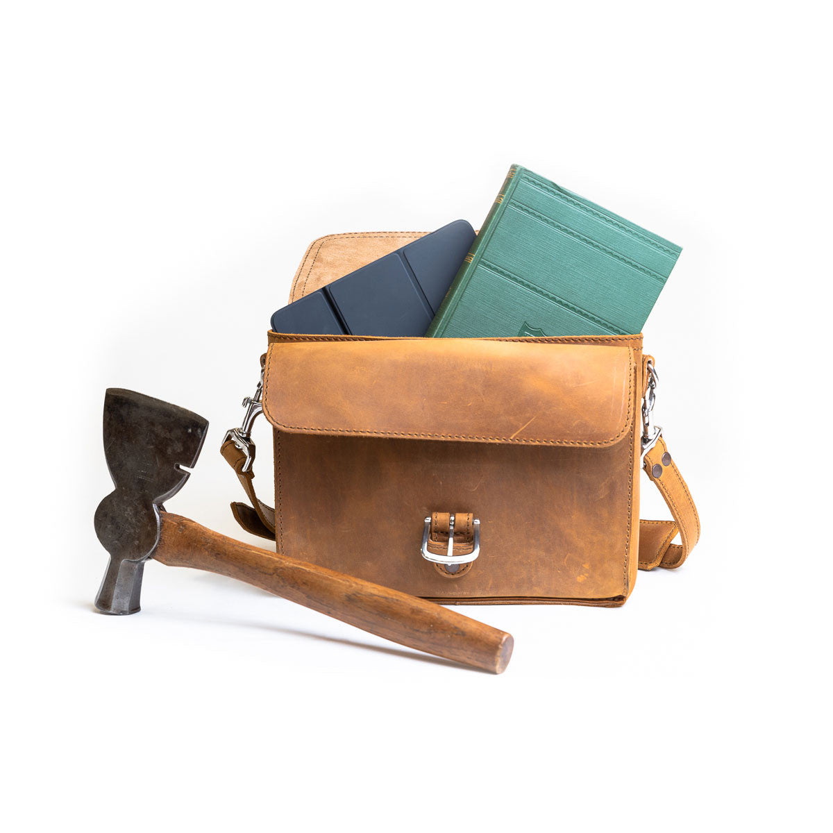 Front Pocket Leather Satchel in Tobacco packed with a tablet and green notebook, beside a vintage hatchet