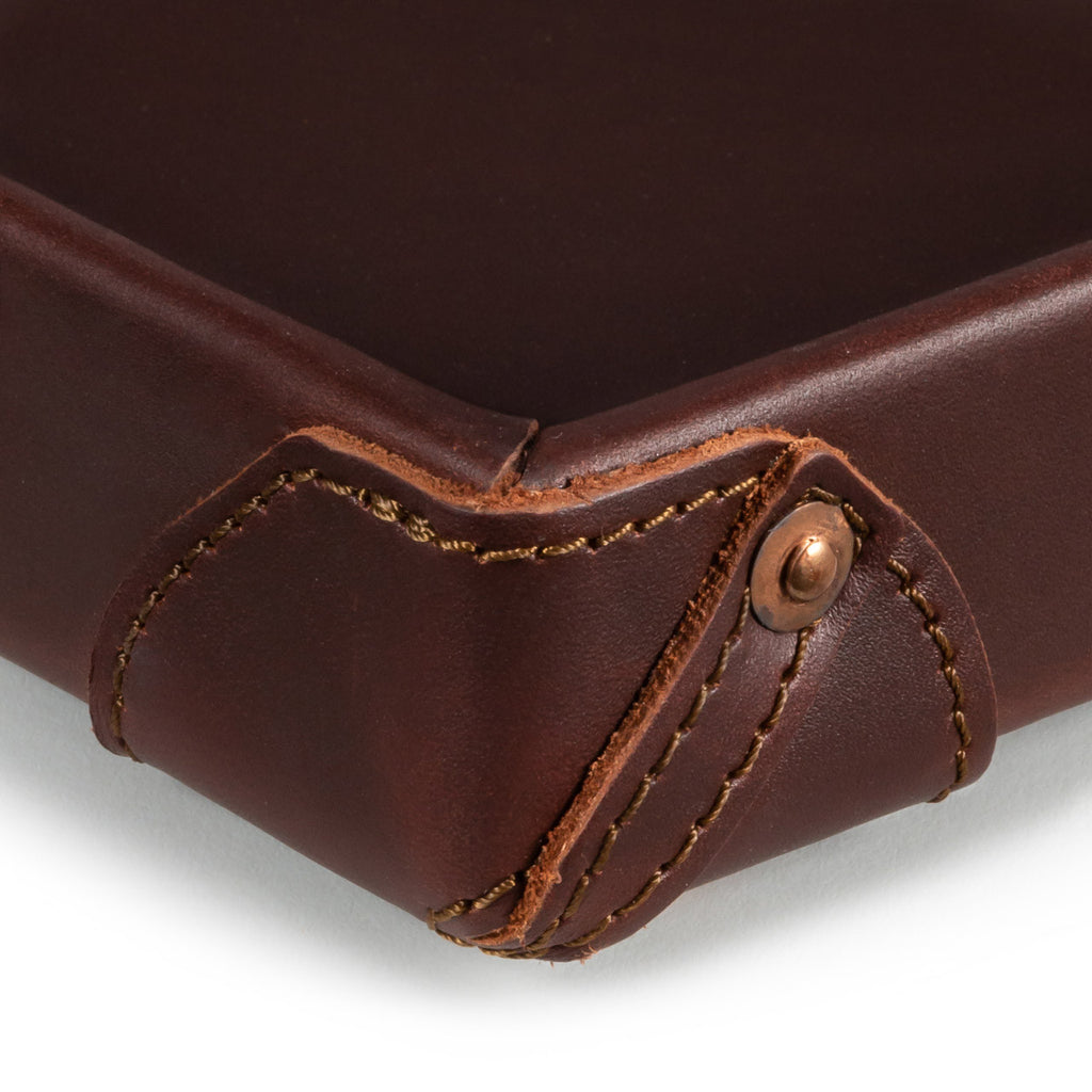 The Leather Grandfather Valet Tray in Chestnut, close-up of a stitched corner tab with copper rivet