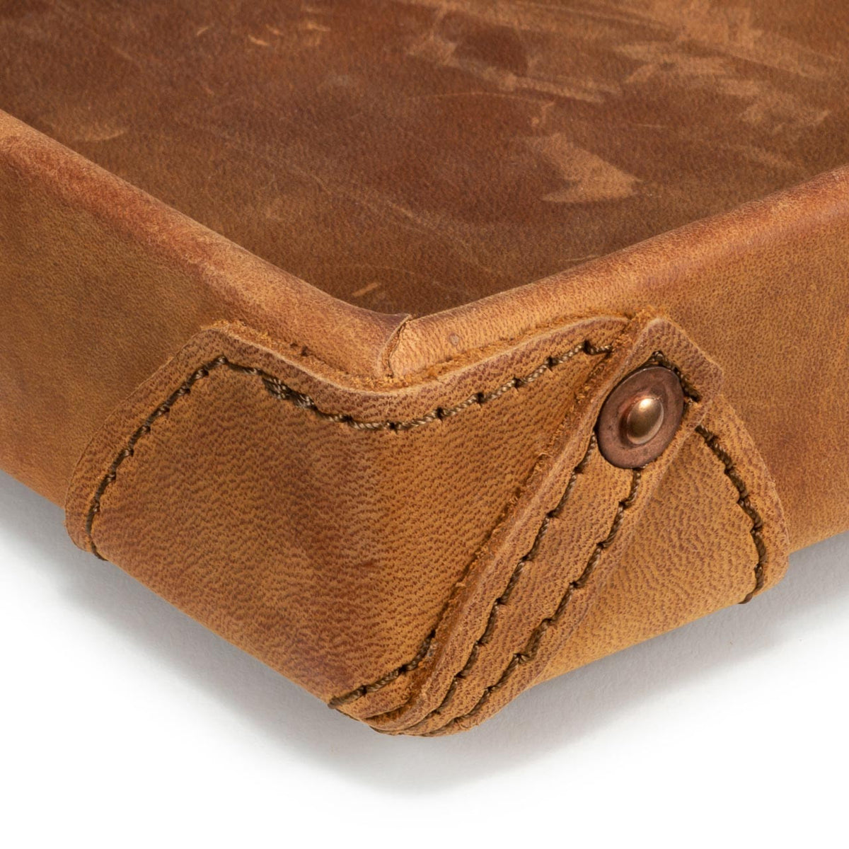 The Leather Grandfather Valet Tray in Tobacco, close-up of a stitched corner tab with copper rivet