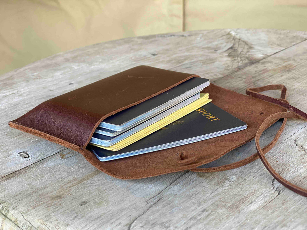 Cash & Receipt Bag in Chestnut, open on a weathered wooden table holding a passport and small notebooks