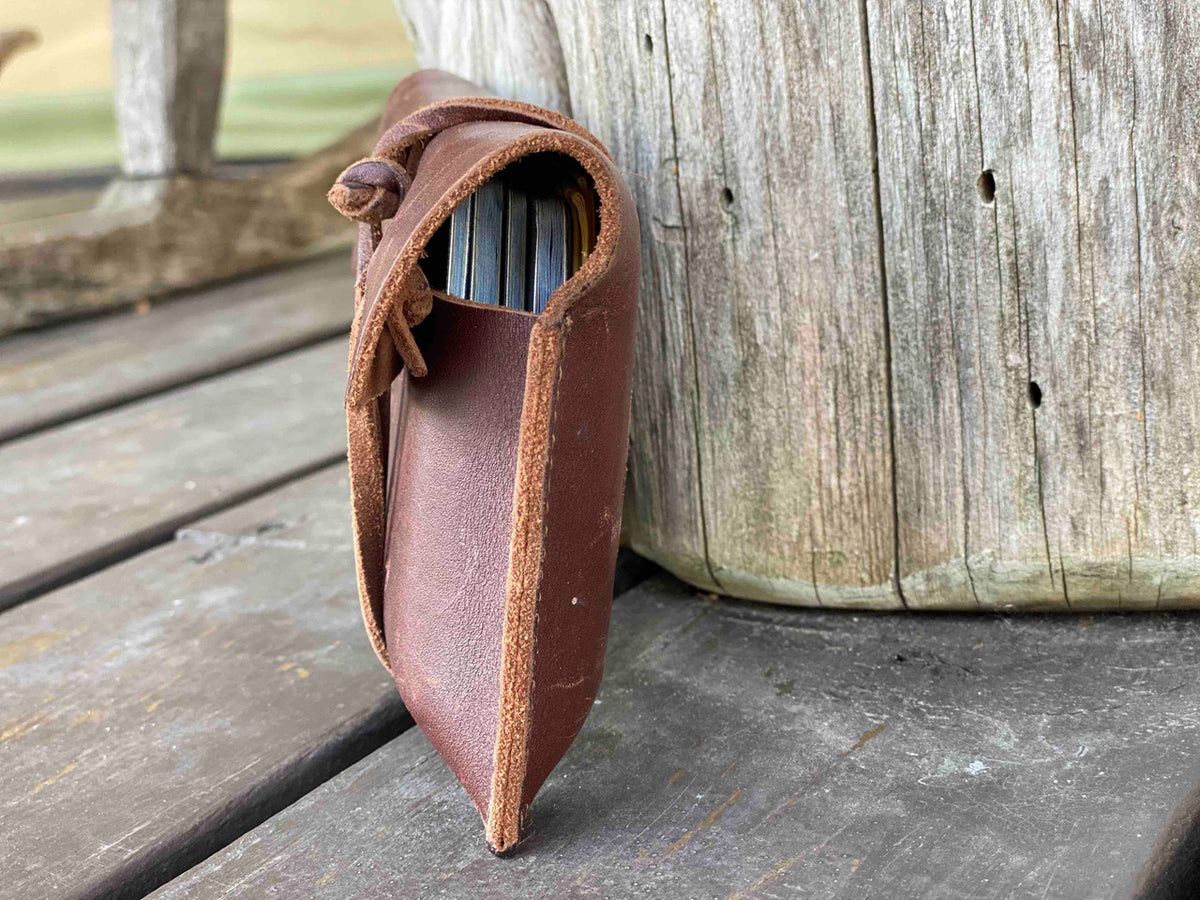 Cash & Receipt Bag in Chestnut standing upright on a weathered wooden deck with items tucked inside