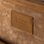 Leather Trunk in Tobacco, close-up of stitched logo patch on the suede interior of the lid