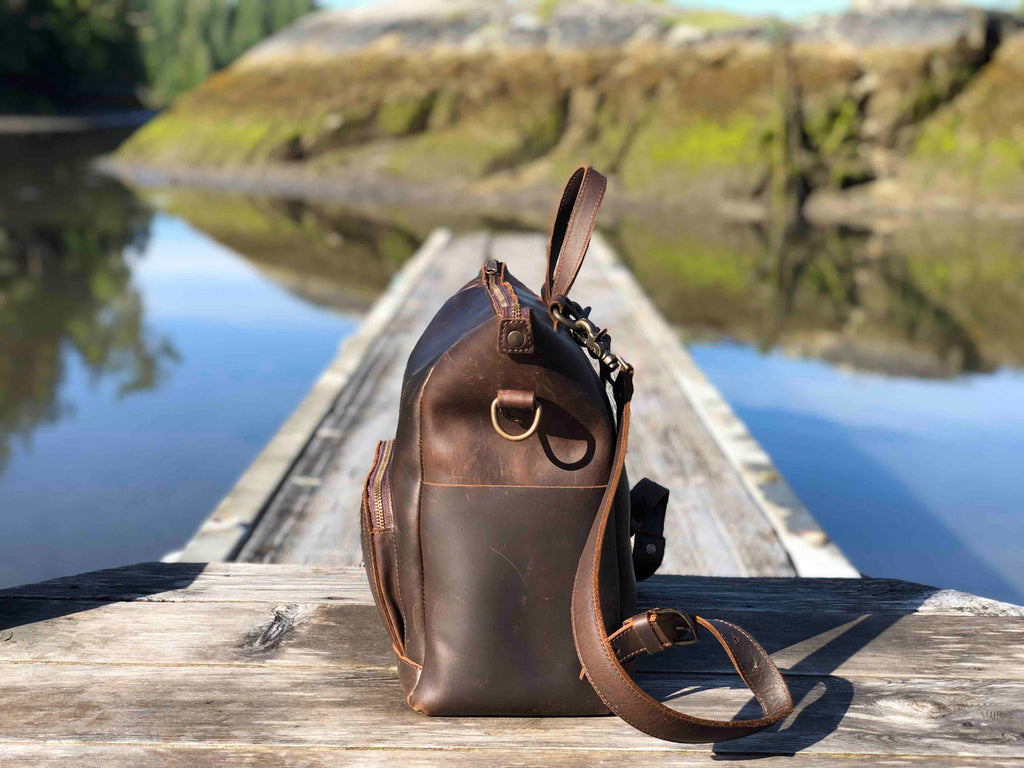 Universal Leather Backpack in Dark Coffee Brown, side profile on a wooden dock over a lake