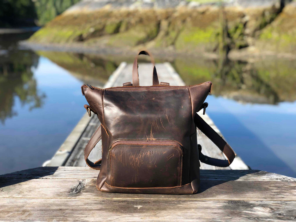 Universal Leather Backpack in Dark Coffee Brown on a wooden dock over a calm lake