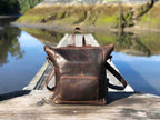 Universal Leather Backpack in Dark Coffee Brown on a wooden dock over a calm lake