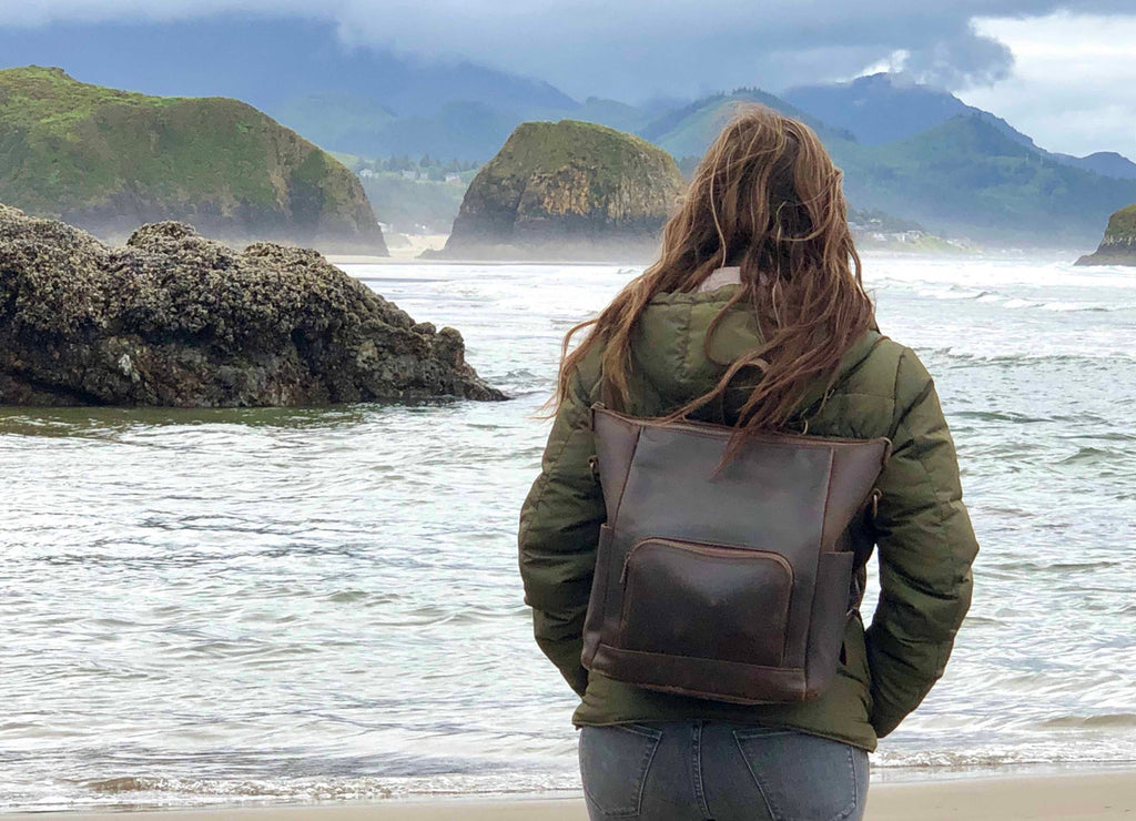 Universal Leather Backpack in Dark Coffee Brown worn by a woman standing at the ocean shore