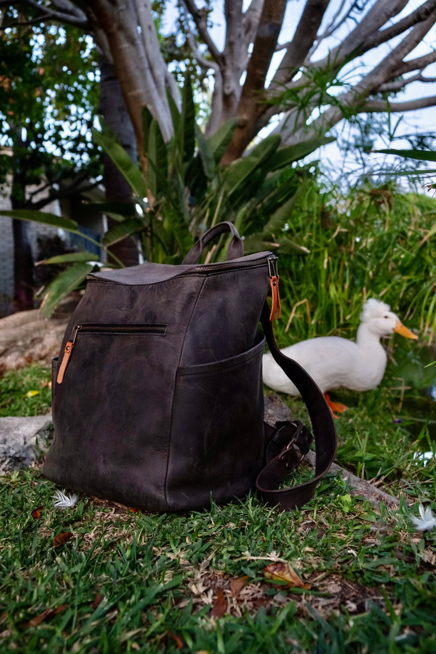 All in One Leather Backpack in Black on the grass with a white duck behind it