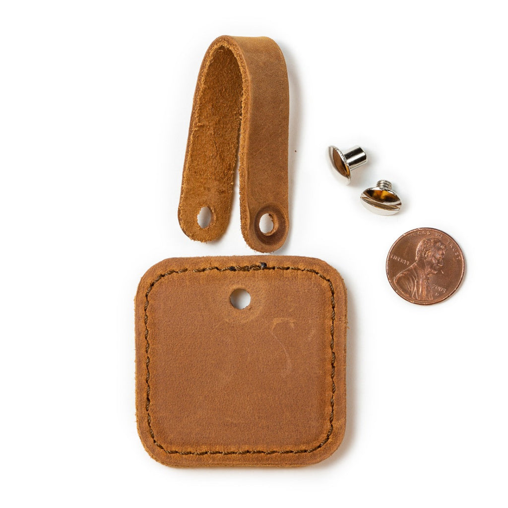 Leather Bag Tag in Tobacco taken apart, showing the strap, tag and screw post next to a penny for scale