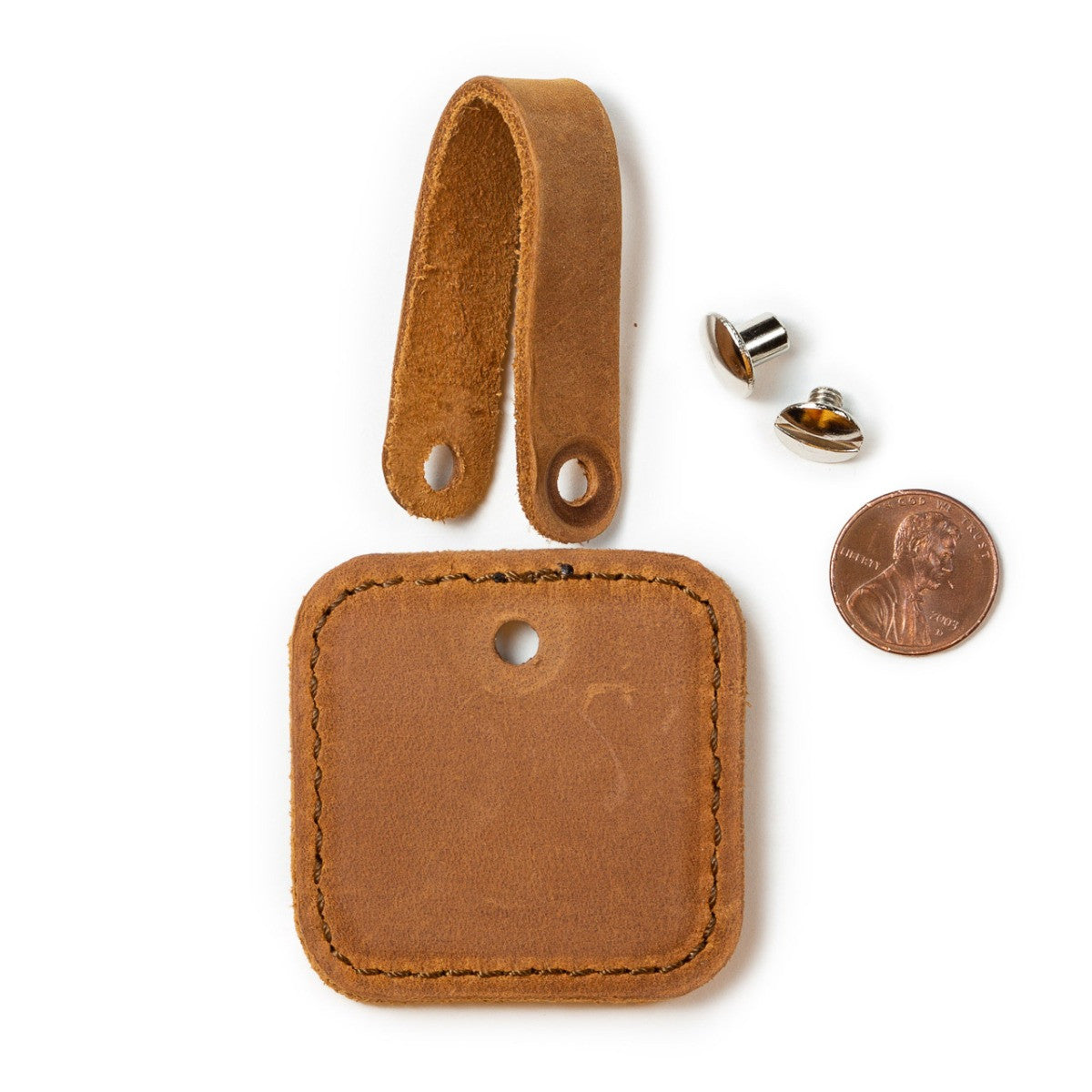 Leather Bag Tag in Tobacco taken apart, showing the strap, tag and screw post next to a penny for scale