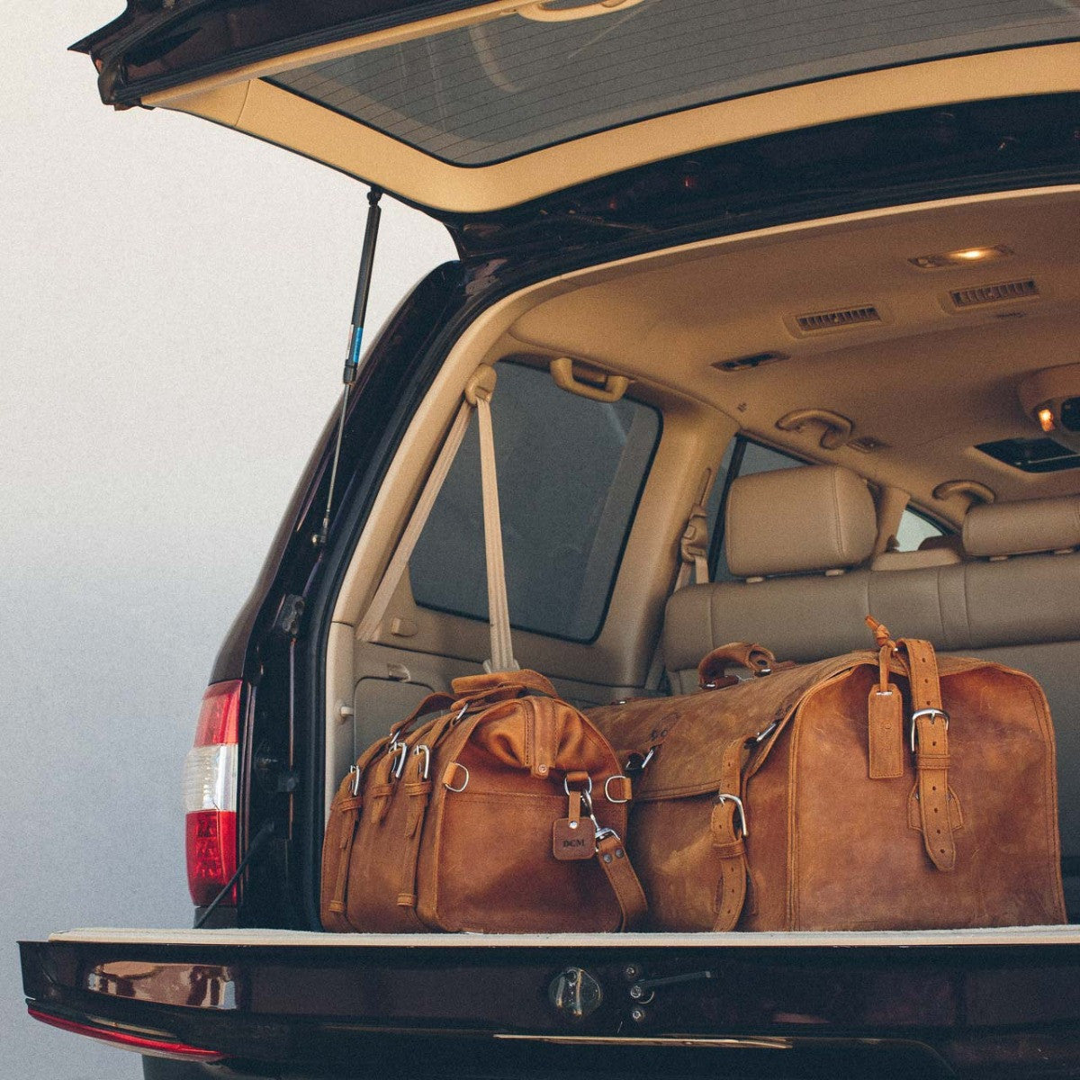Leather Bag Tag in Tobacco on a leather duffel bag, two Tobacco duffels in the back of an SUV
