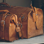 Leather Bag Tag in Tobacco with DCM monogram hanging from a Tobacco leather duffel bag, close-up
