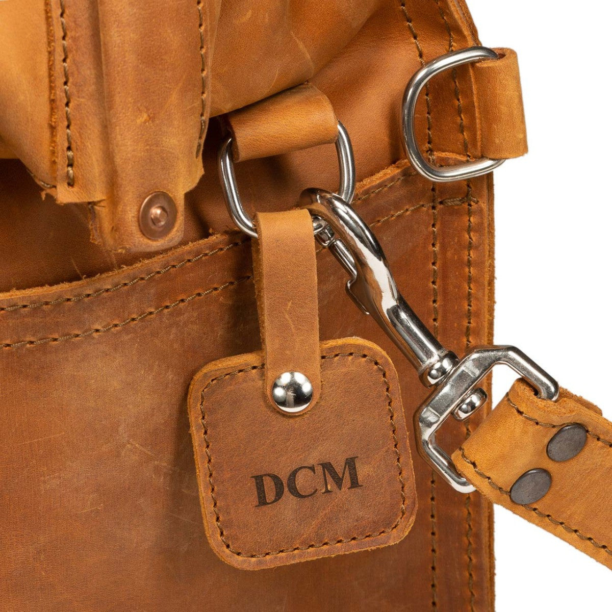 Leather Bag Tag in Tobacco with DCM monogram on a D-ring beside a strap swivel hook, close-up