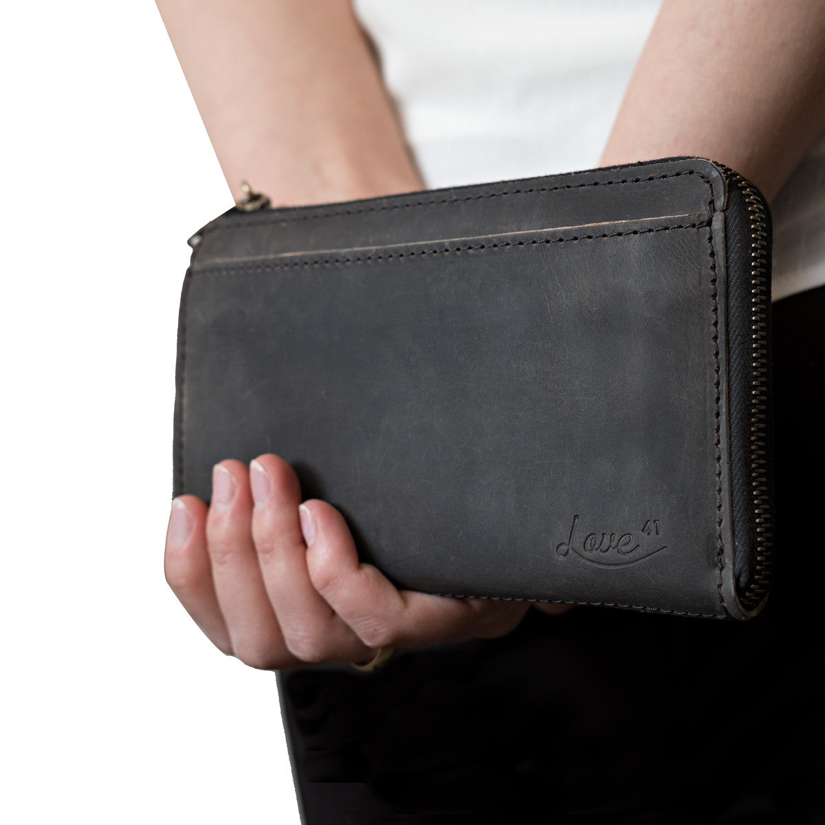 Medium Wristlet Leather Wallet in black, held in hand showing front pocket and embossed logo