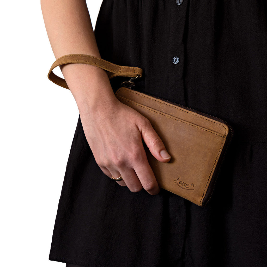Medium Wristlet Leather Wallet in tan, held in hand with strap around wrist against a black dress