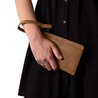 Medium Wristlet Leather Wallet in tan, held in hand with strap around wrist against a black dress