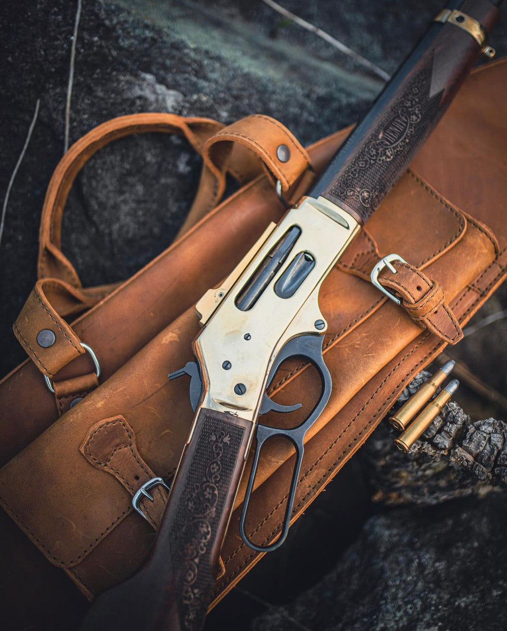 Shotgun Sleeve in Tobacco on a rock with a brass-framed lever-action rifle and cartridges resting on top