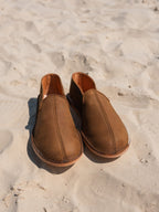 Pair of Barefoot Slip-on Shoes in Tobacco standing on sand, front view