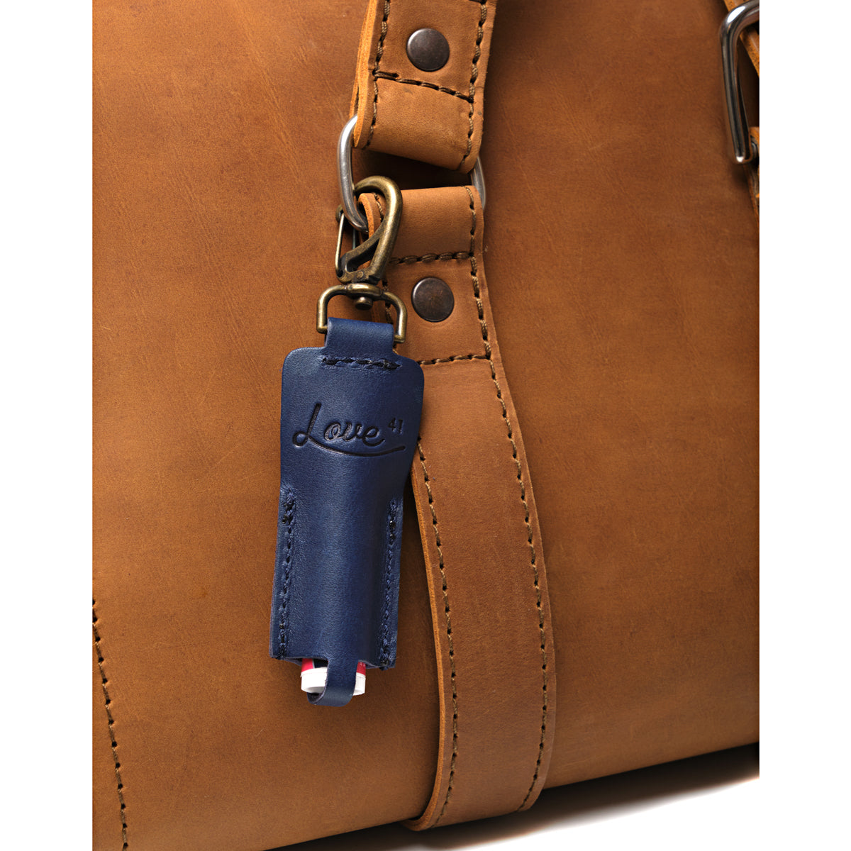 Leather Chapstick Holder in navy blue, clipped to the strap ring of a tan leather bag