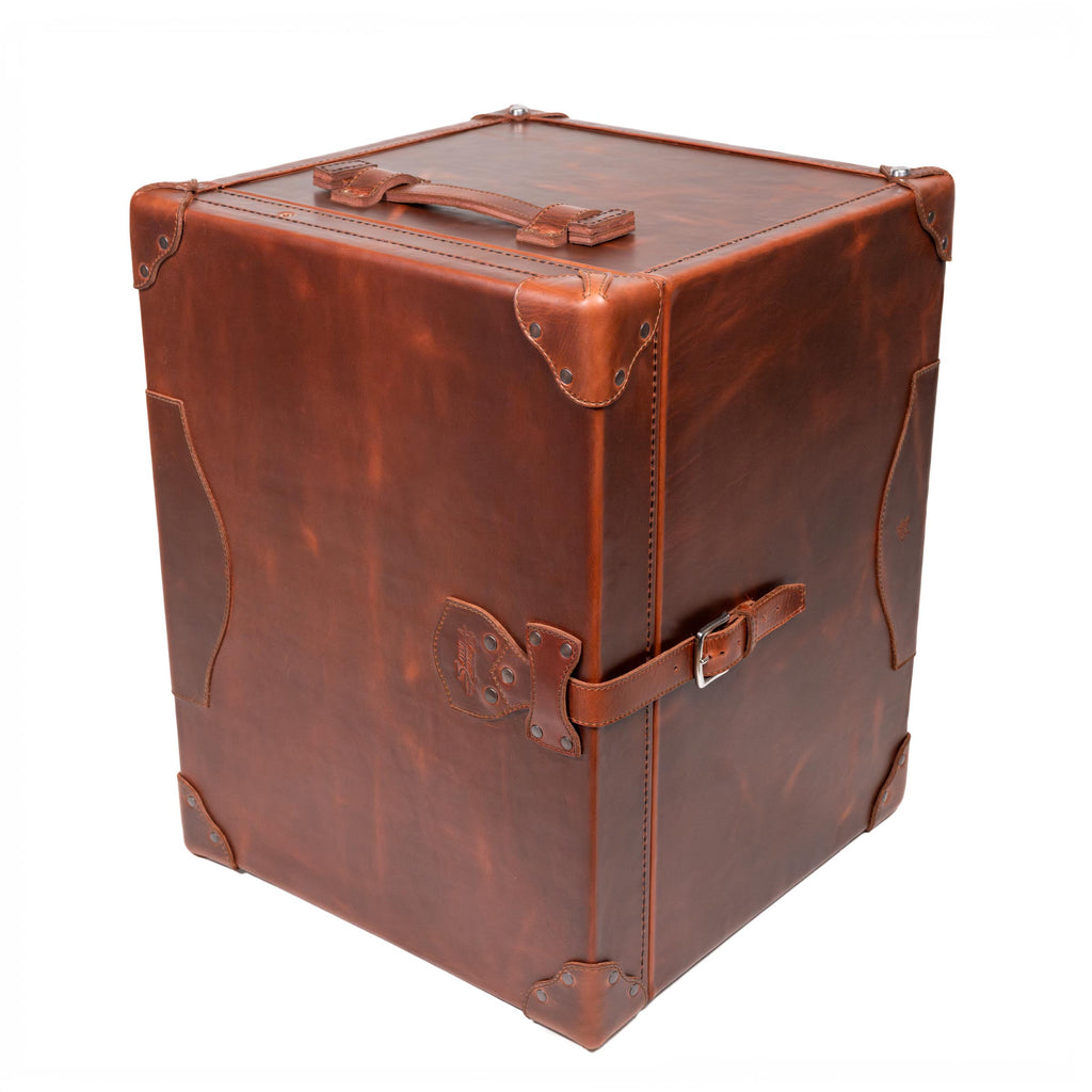 Leather Small Trunk in Chestnut, standing upright and closed with top handle, buckled strap and corner guards