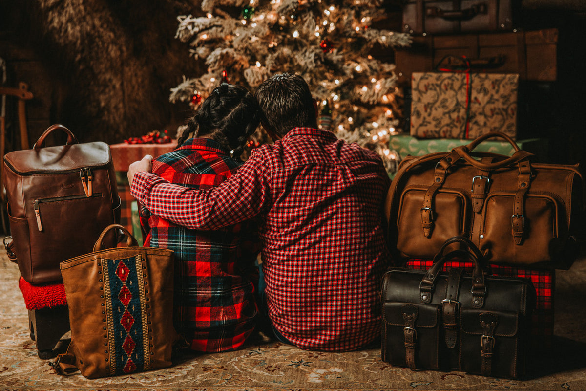 Lanita Leather Backpack lifestyle, couple by a Christmas tree surrounded by leather bags including the woven backpack