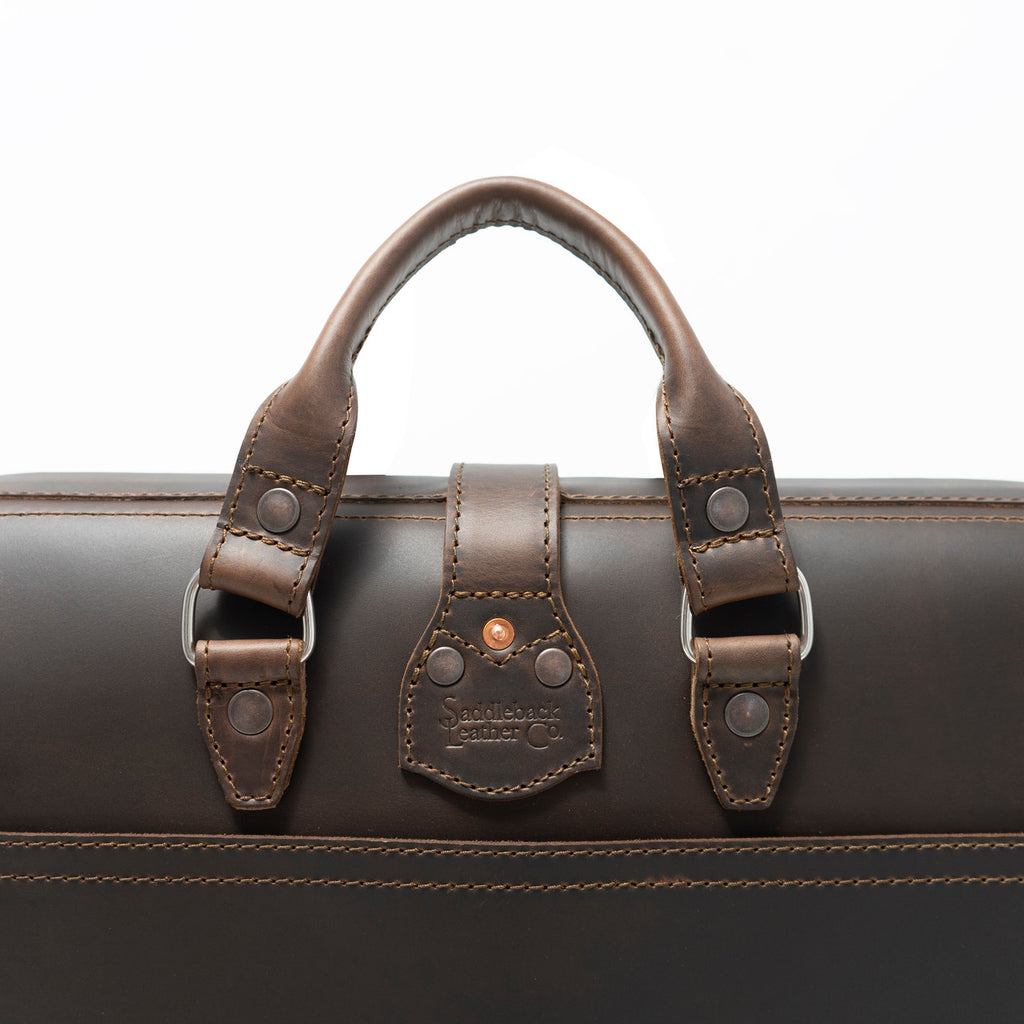 Flight Bag Leather Briefcase in dark brown, close-up of the top handle and riveted tab with embossed Saddleback Leather Co. logo