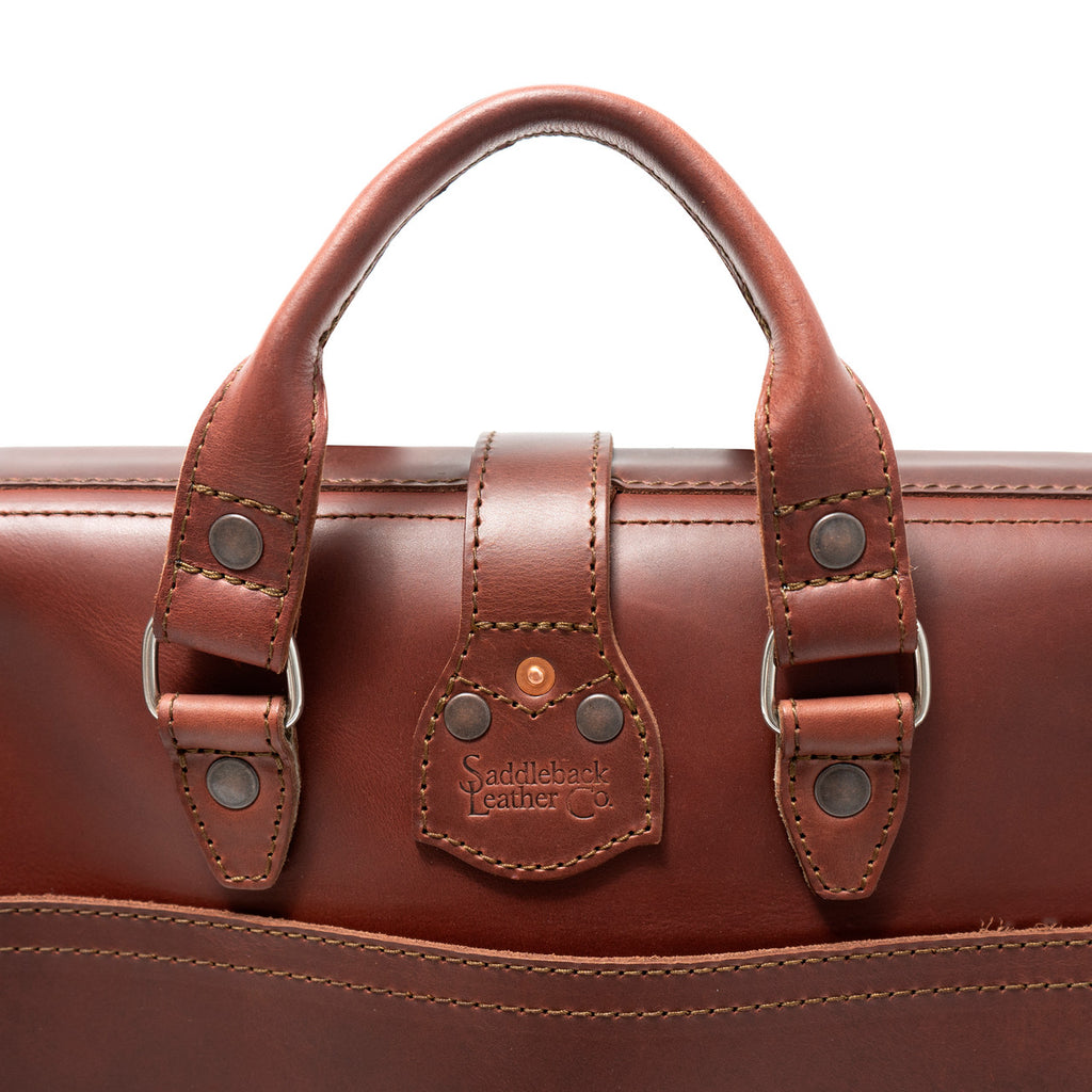 Flight Bag Leather Briefcase in chestnut, close-up of the top handle and riveted tab with embossed Saddleback Leather Co. logo