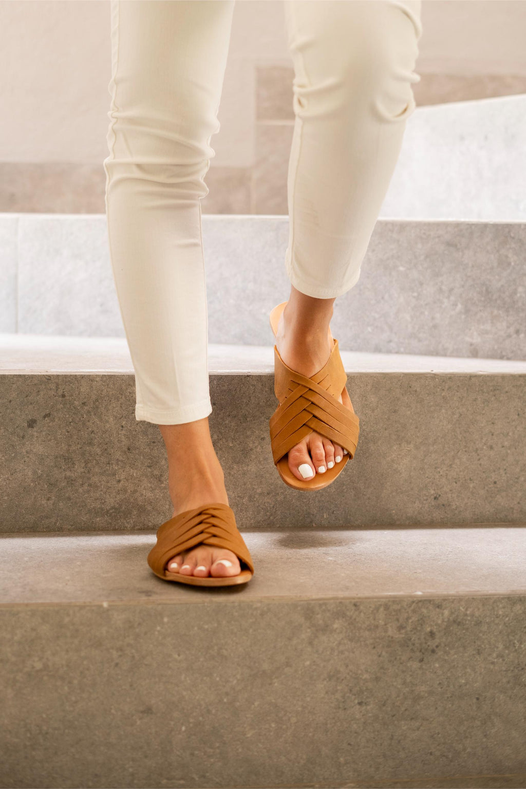 Martha Sandals in Tobacco worn with cream pants while walking down concrete steps